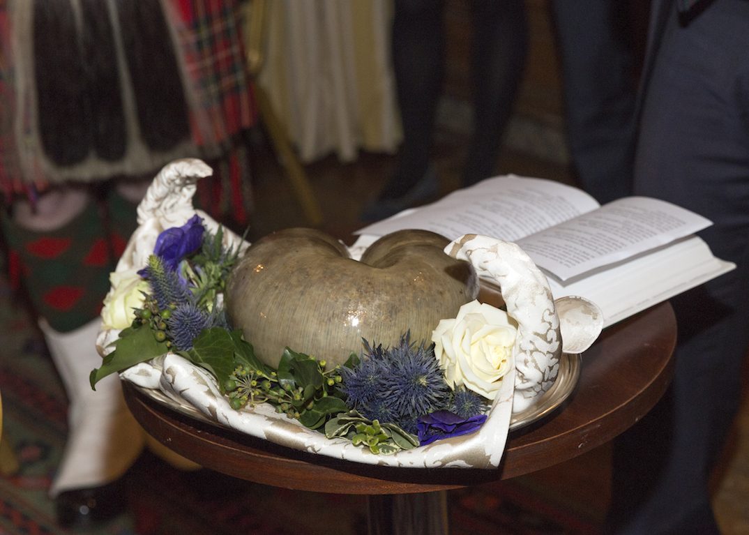 A haggis on a silver platter with thistles and a book of Burns's poems at a Burns supper